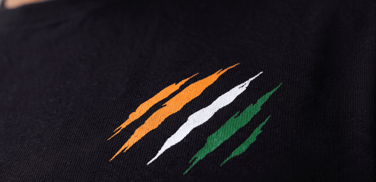 Close-up of a black knit garment featuring a stylized embroidered claw-mark graphic in orange, white, and green on the chest.