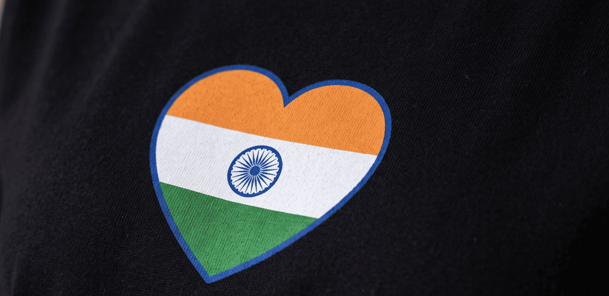 A close-up of a black fabric item, likely a t-shirt, featuring a heart-shaped patch printed with the Indian national flag.