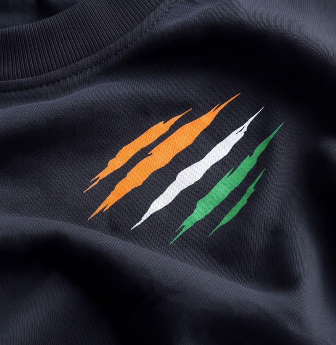 Close-up of a black t-shirt featuring a graphic of three diagonal scratch-like stripes in orange, white, and green.