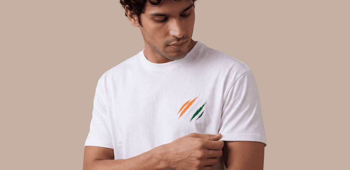 A man wearing a white crew-neck t-shirt with a small orange and green graphic on the left chest, set against a solid beige background.