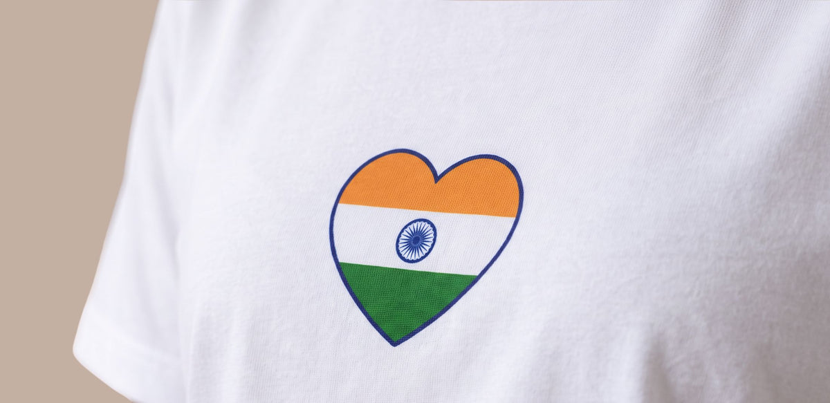 A close-up of a white t-shirt featuring a heart-shaped graphic printed with the Indian flag (saffron, white, and green with the Ashoka Chakra).
